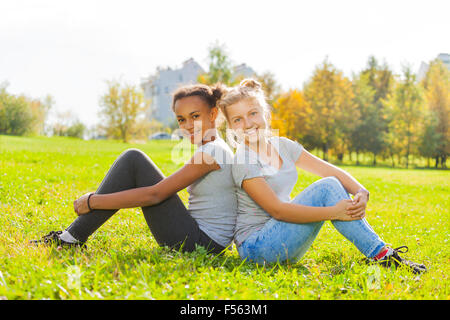 E africano ragazza bionda seduta insieme sull'erba Foto Stock