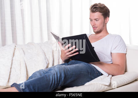 Ritratto giovane uomo seduto sul divano e la lettura di un libro Foto Stock