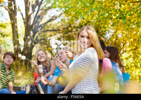 Ragazza e amici con bastoni di marshmallow seduta Foto Stock