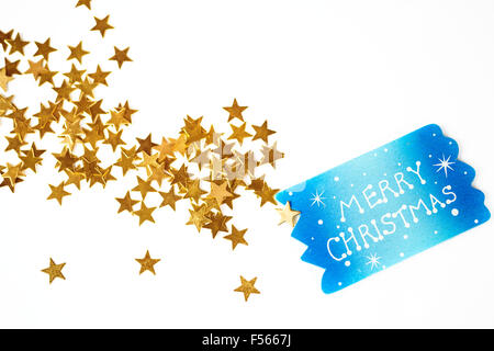 Sfondo di natale con un piccolo cartello blu con i saluti e un po' di Golden Stars alla rinfusa su sfondo bianco Foto Stock