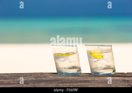 Bicchieri di acque con il limone su legno su sfondo del mare Foto Stock