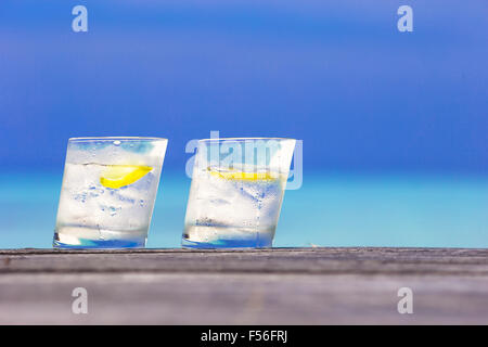 Bicchieri di acque con il limone su legno su sfondo del mare Foto Stock
