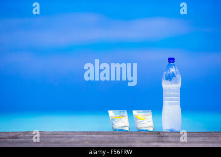 Bicchieri di acque con limone e bottiglia in legno su sfondo del mare Foto Stock
