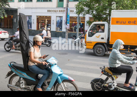 Hanoi, Vietnam, attraente ragazza scooter di equitazione mentre si utilizza il telefono cellulare e la ragazza su scooter elettrico con maschera facciale. Foto Stock