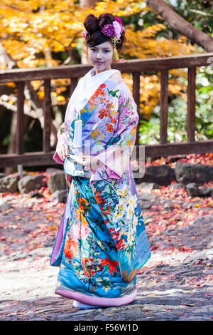 Il Giappone. Le donne giapponesi in kimono nuziale prosing esterno sul lasciare il percorso coperto durante l'autunno. Vista laterale, girato verso la faccia. Contatto visivo. Foto Stock