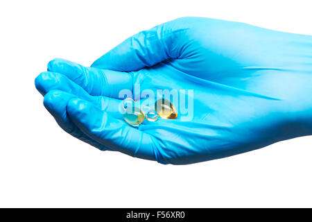 Close up Capsule soft gel con colore dorato dei supplementi di olio sulle donne medico la mano in blu sterilizzato guanto chirurgico contro Foto Stock