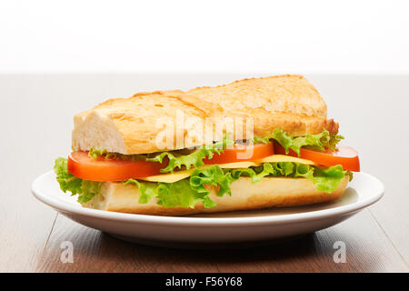 Pomodoro, formaggio e insalata panino da baguette fresca sul piatto di portata in ceramica bianca sul luminoso in legno marrone chiaro dello sfondo della tabella Foto Stock