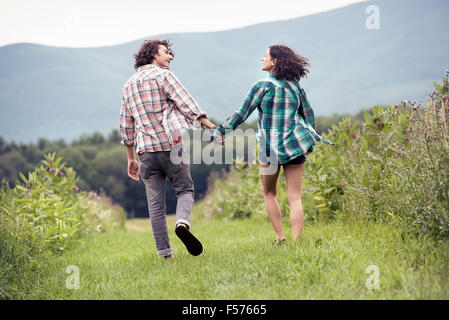 Un giovane uomo e donna in esecuzione attraverso un prato di mano in mano. Foto Stock