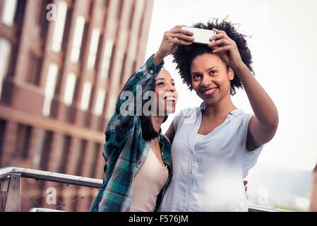 Due donne in posa e prendendo un selfie da un grande edificio nella città Foto Stock