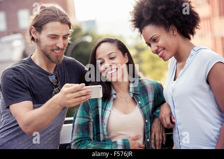 Due donne e un uomo in cerca di un telefono intelligente Foto Stock