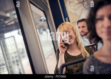 Una donna bionda su un autobus di città, parlando sul suo smart phone Foto Stock