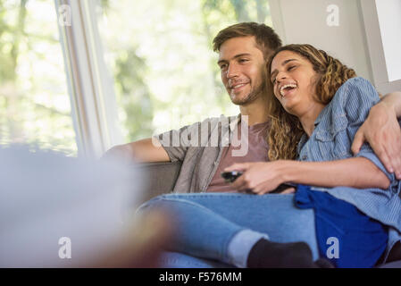 Una coppia di uomo e donna seduta a fianco a fianco di ridere, guardando una schermata. Foto Stock