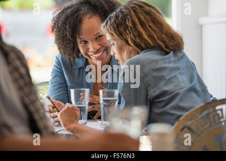 Tre persone seduti ai tavoli in una caffetteria. Conversazione tra due donne e guardando uno smart phone. Foto Stock