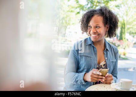 Una donna che mantiene il suo smart phone, presso una caffetteria tabella. Foto Stock