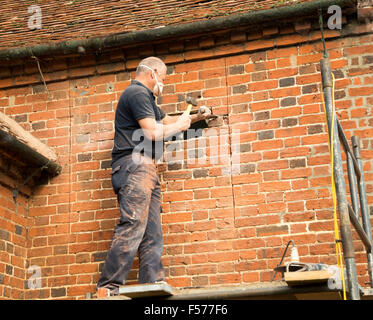 Builder rimozione di mattoni rossi per fare spazio nella finestra, Suffolk, Inghilterra, Regno Unito Foto Stock