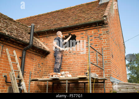 Builder rimozione di mattoni rossi per fare spazio nella finestra, Suffolk, Inghilterra, Regno Unito Foto Stock