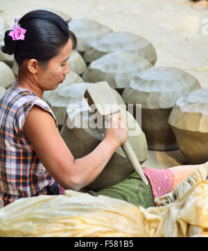 La donna nel villaggio di Irrawaddy vicino a Mandalay battendo in argilla vasi d'acqua in forma con una paletta di legno . Foto Stock