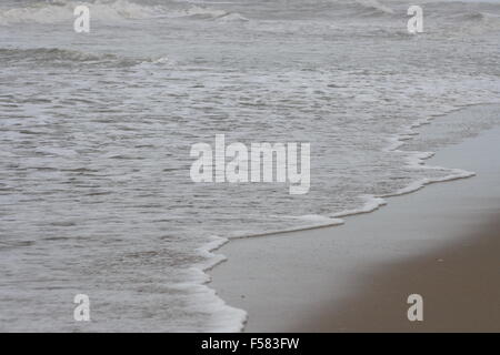 Onde con creste bianche inondare la spiaggia sabbiosa Foto Stock