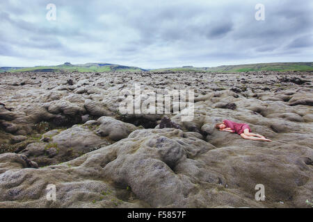 Bella ragazza in abito rosso dormendo nel campo di lava in Islanda, solitudine concept Foto Stock