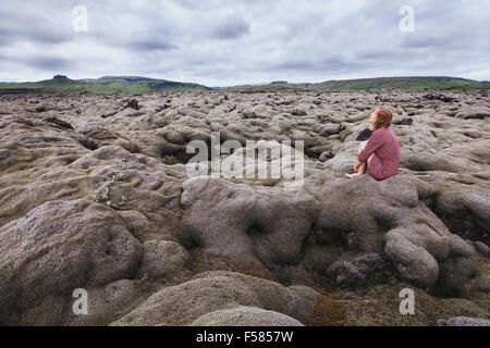 Donna seduta da sola nel campo di lava, guardando il cielo e il pensiero circa il significato della vita Foto Stock
