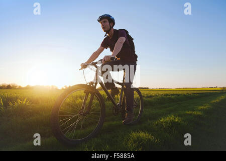 Giovane uomo sportivo equitazione bicicletta all'aperto al tramonto Foto Stock