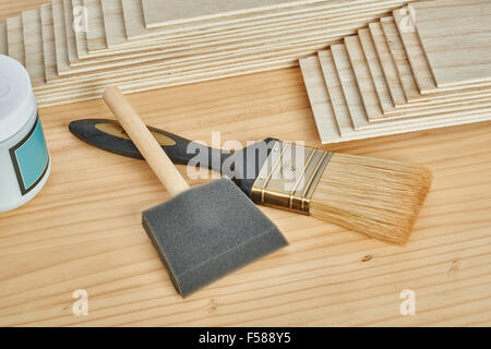 Carpenteria e strumenti di pittura, come titolare di carta vetrata, stack di impiallacciature e pennelli, su un piano di lavoro Foto Stock
