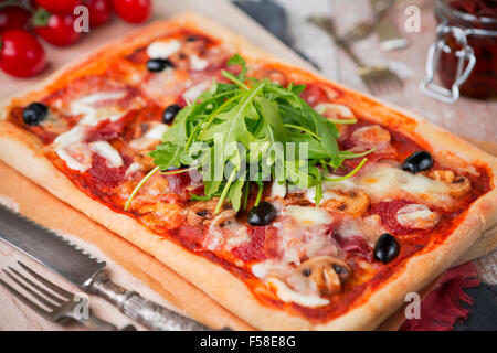 In casa rettangolare di salsiccia per pizza pizza su un tavolo rustico con ingredienti. Foto Stock