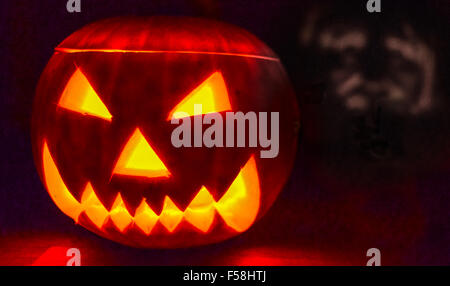 Scary Halloween zucca illuminata da una candela con un volto spettrale ombra dietro. Foto Stock