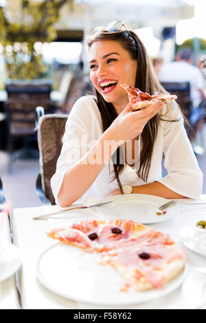 Bella giovane donna di mangiare un trancio di pizza in un ristorante all'aperto Foto Stock