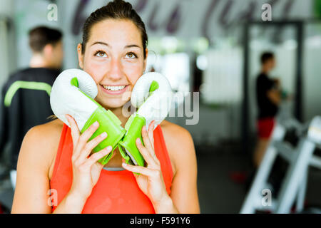 Giovane bella donna sorridente e posa con guantoni da pugilato in una palestra Foto Stock