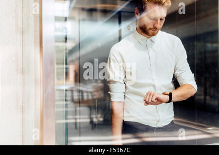 Imprenditore controllo guardare mentre in piedi in vetro ricoperto ascensore Foto Stock