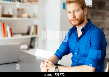 Fiducioso lo zenzero imprenditore seduto alla scrivania in ufficio in una maglietta blu Foto Stock