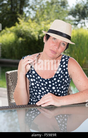 Donna attraente siiting presso la piscina e il fumo e-sigaretta Foto Stock