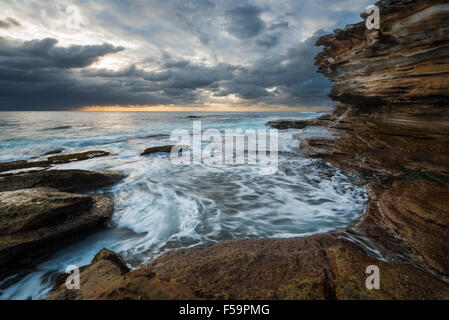 Seascape alba con disordini mare e cielo grim e scogliere Foto Stock