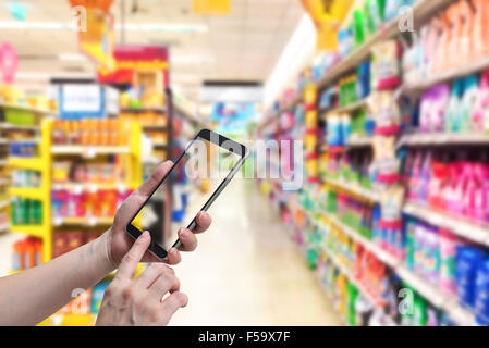 La doppia esposizione tenere in mano e il touch screen smart phone, tablet,cellulare più sfocato shopping center o super mercato sullo sfondo Foto Stock