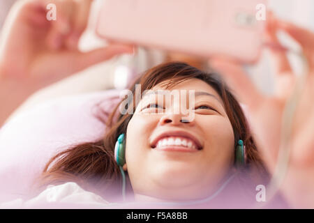 Asian giovane ragazza utilizzando smart phone indossare le cuffie Foto Stock