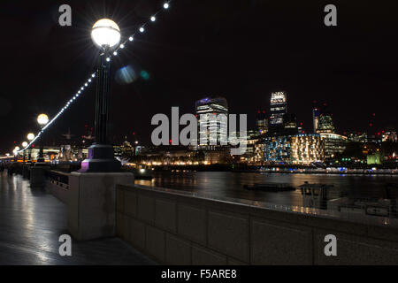 Il fiume Tamigi passando tranquillamente davanti ad un luminoso sullo skyline di Londra di notte Foto Stock