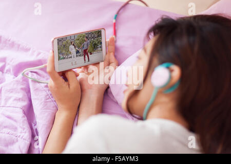 Asian giovane ragazza guarda video mobile smart phone indossare le cuffie Foto Stock