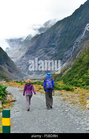 Due escursionisti che camminano lungo un percorso roccioso lungo il fiume vicino al ghiacciaio fondono l'acqua fino alla Toe dell'Isola Sud del ghiacciaio Franz Josef, Nuova Zelanda Foto Stock