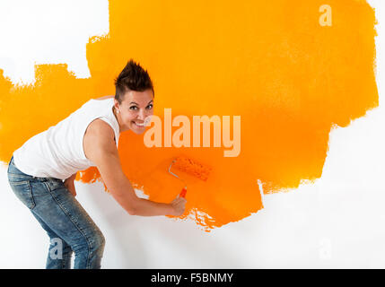 Bella Donna informale di verniciatura di un muro bianco con colore arancione. Lei sta cercando la fotocamera con un sorriso amichevole. Foto Stock