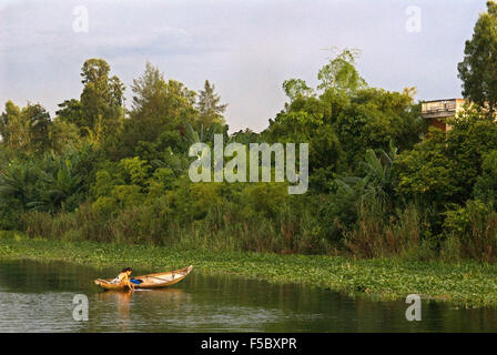 Bella ragazza pulire i vestiti all'interno di un sampan in legno rende la sua strada verso il brown acque del fiume Perfume in tinta, Vietnam. Foto Stock