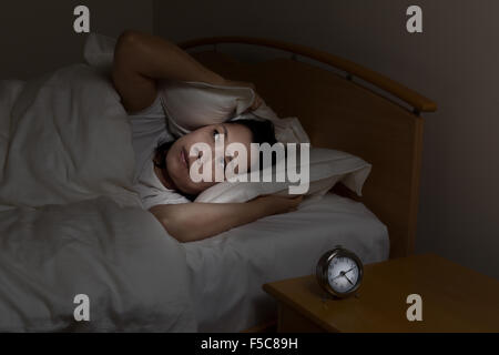 Donna con insonnia che copre le sue orecchie con cuscino mentre gli occhi aperti. Selezionare luce e concentrarsi sulla donna con sfondo scuro Foto Stock