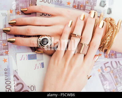 Le mani della donna ricca con golden manicure e molti gioielli anelli sul cash euro close up Foto Stock