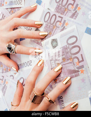 Le mani della donna ricca con golden manicure e molti gioielli anelli sul cash euro close up Foto Stock