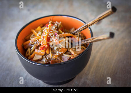 Stir fry con carne e verdure, guarnito con semi di sesamo nella ciotola con bacchette. Tradizionale cucina asiatica Foto Stock