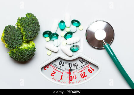 La dieta mangiare sano controllo del peso e per la cura della salute concetto. Closeup broccoli verdi stetoscopio in pillole su scale di bianco, scelta tra Foto Stock