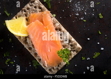 Salmone affumicato su cracker integrale con il prezzemolo, limone e sale Foto Stock