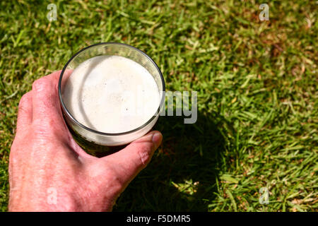 Man mano che tiene una pinta bicchiere di birra amaro al di fuori in estate Foto Stock