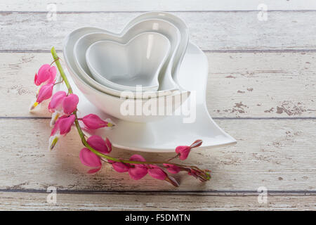 Un Nido di bianco a camma a forma di cuore piatti in ceramica su di una  corrispondente piastra con uno spruzzo di un bel colore rosa cuore di  spurgo fiori Foto stock 