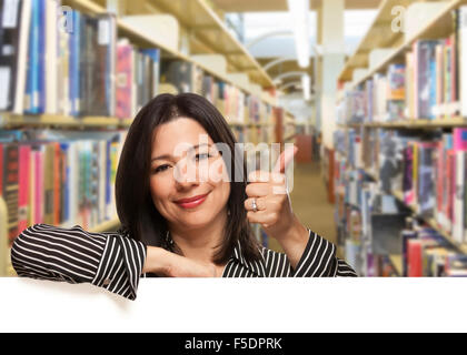 Bella Donna ispanica con il pollice su appoggiato su una lavagna bianca nella libreria. Foto Stock